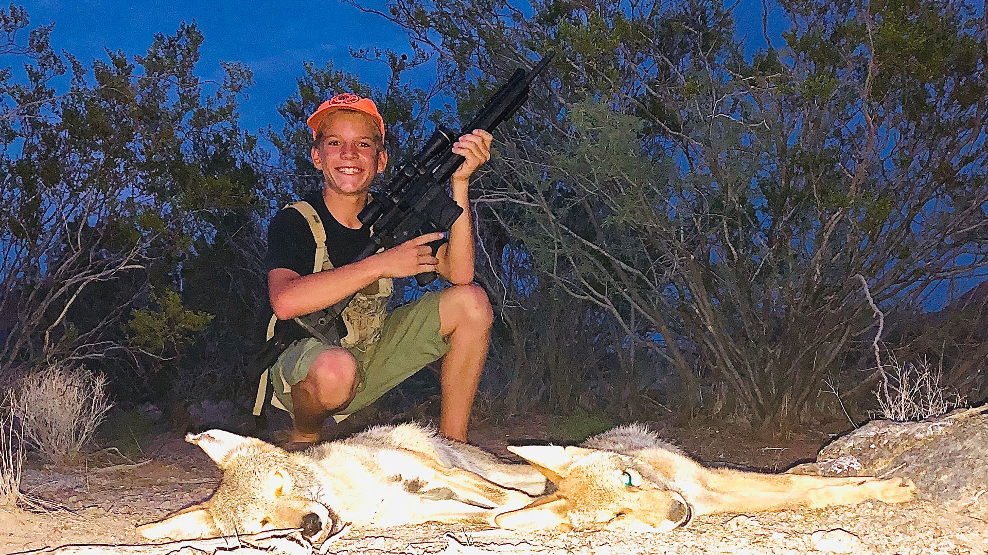 Young hunter poses over pair of coyotes with rifle
