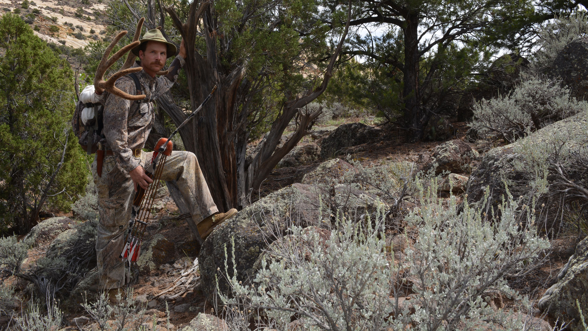 Bowhunter with muley head on back stands posed on a rock