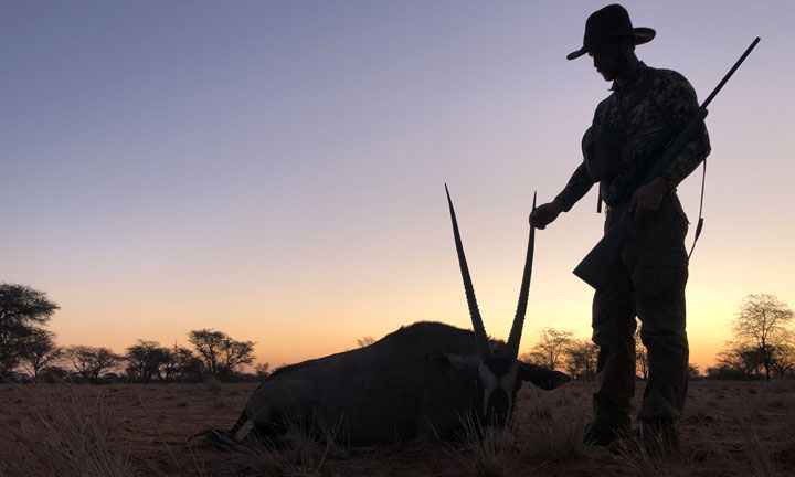Hunter stands silhouetted against the African sunset with a downed animal.