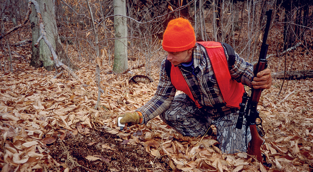 Hunter spreading deer scent on ground.