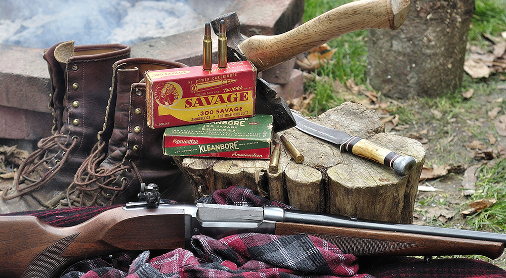 Savage Model 99 rifle with .300 Savage ammunition and leather boots near wood pile.