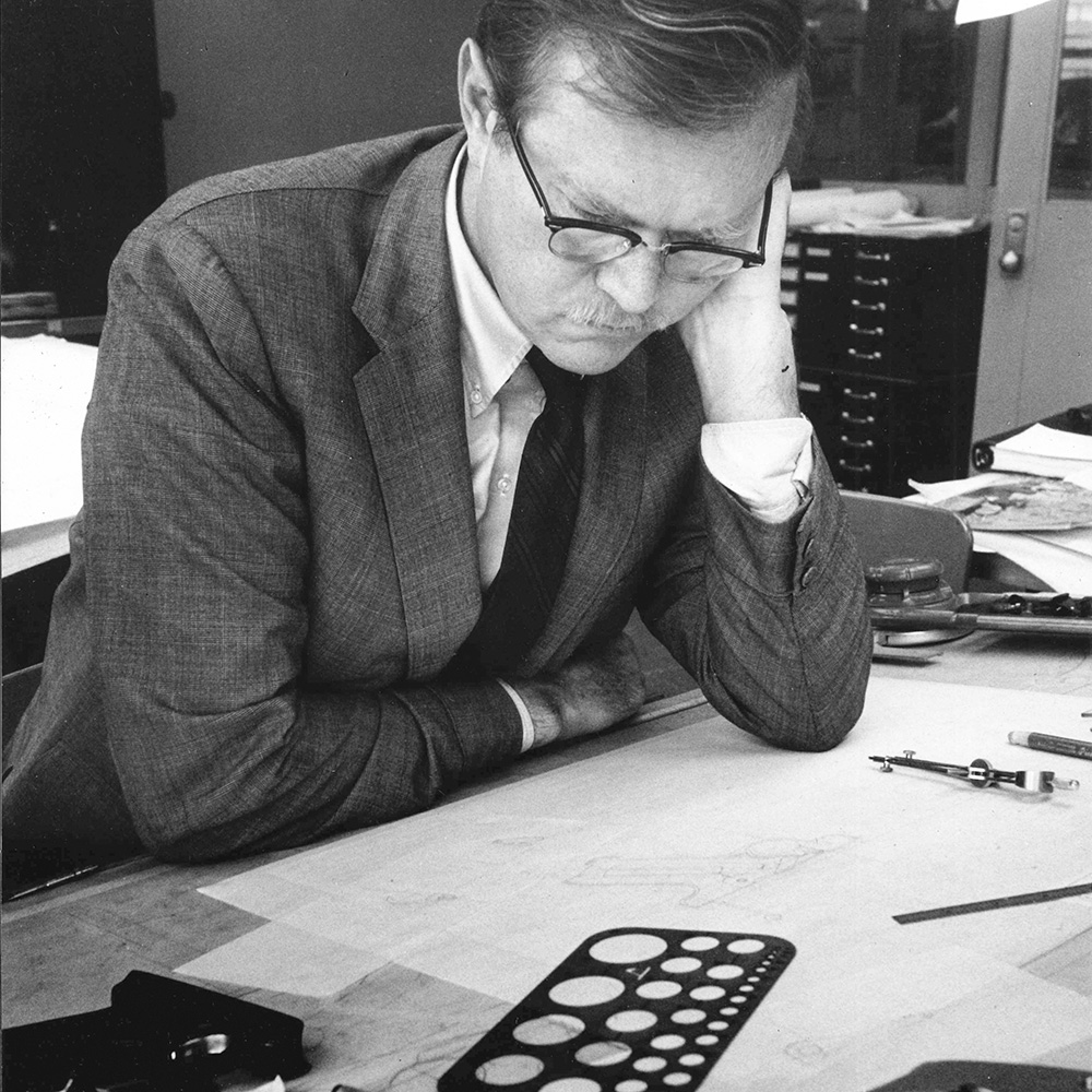 Bill Ruger sitting at desk pondering drawing of handgun.