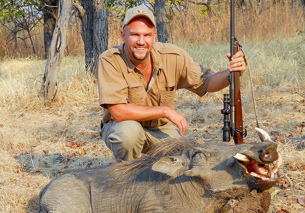 Male hunter posing with warthog in Africa.