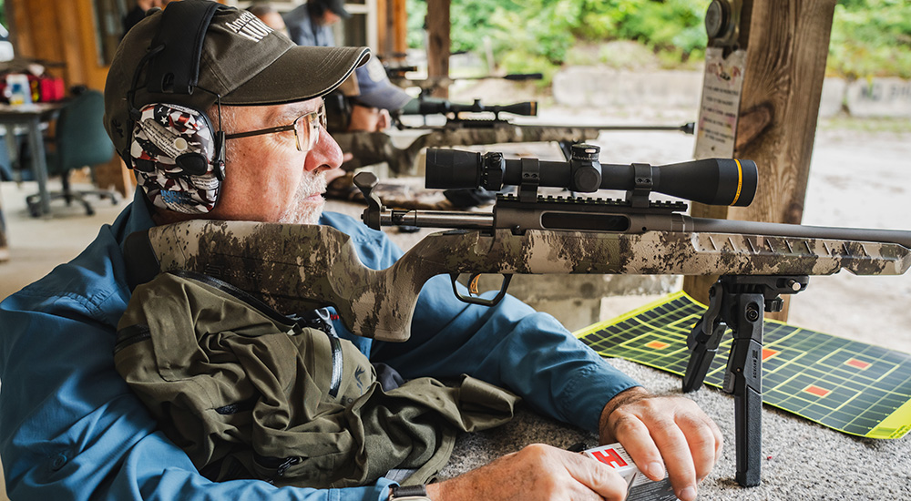 Male at shooting bench with Savage Axis 2 Pro rifle shouldered.