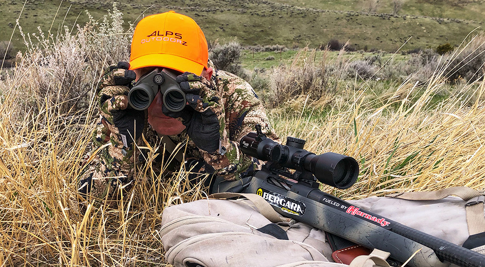 Hunter looking through binoculars in tall grass.