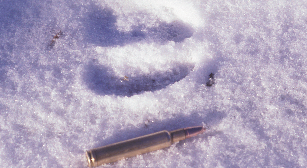 Single round of ammunition next to deer track in snow.