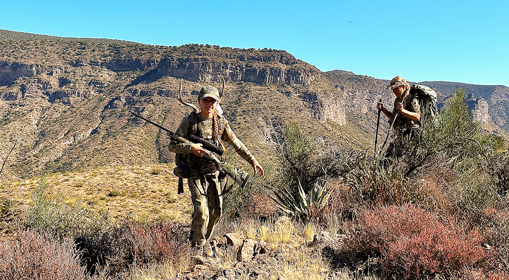 Young female hunter carrying Kimber Mountain Ascent rifle in mountains.