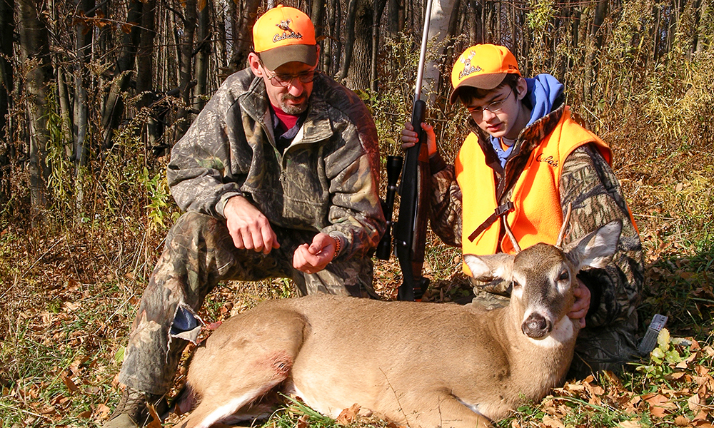 Two male hunters posing with young whitetail buck.