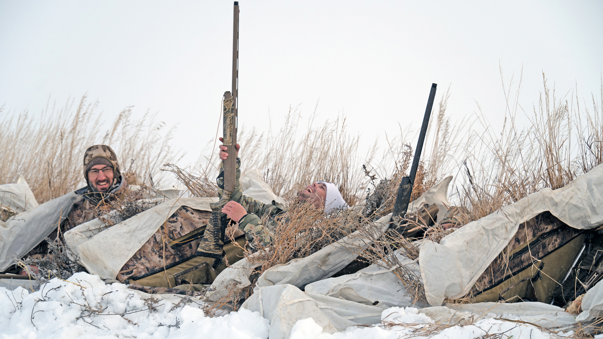 Happy hunters in snow grass holding shotguns goose hunting overcast sky