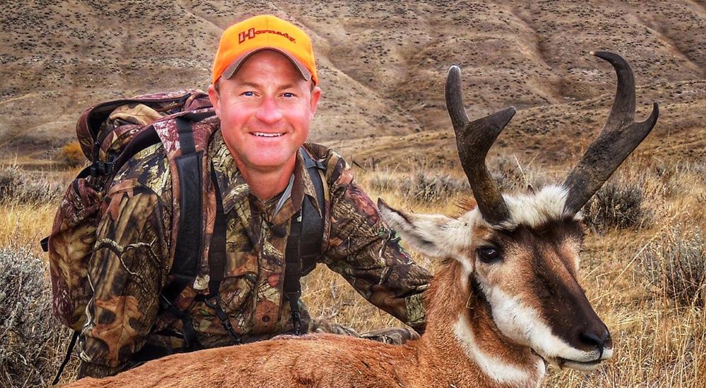 Male hunter posing with pronghorn antelope in open Western terrain.