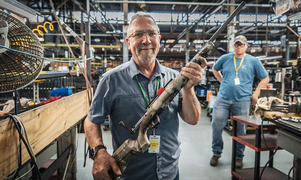 Male holding Savage Axis 2 bolt action rifle in Savage factory.