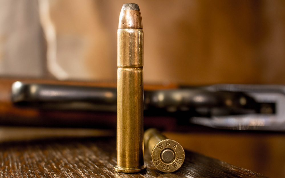 Two rounds of .38-55 Winchester ammunition on wood table.