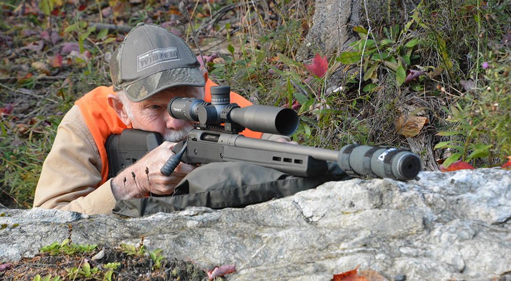 Adult male hunter shouldering bolt action rifle rested on rock.