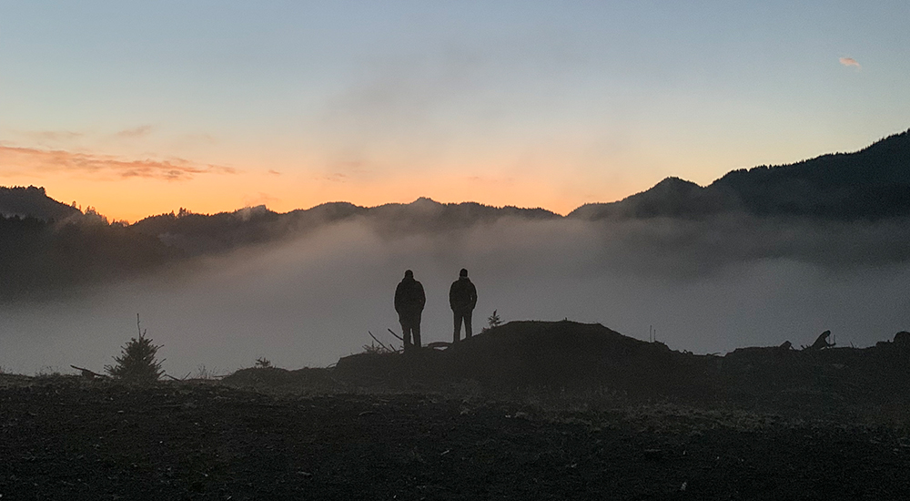 Two male hunters standing on mountain horizon at sunrise in Oregon.