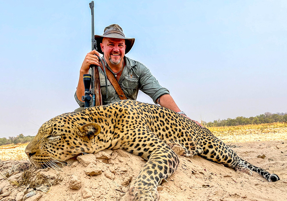 Hunter posing with leopard in Africa holding Todd Ramirez custom rifle.