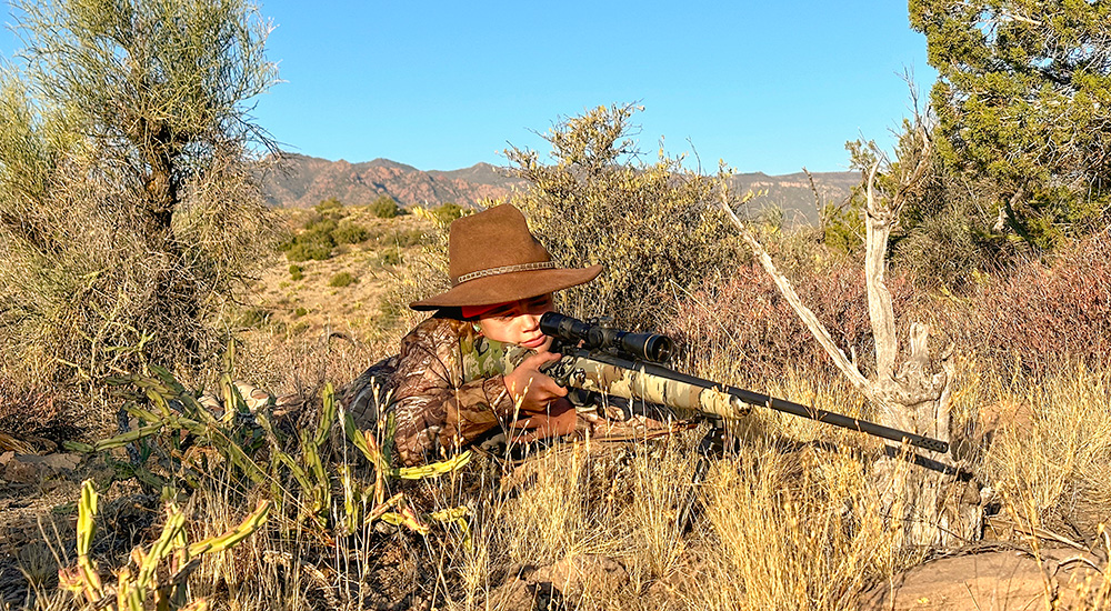 Young female hunter on mountain top with rifle shouldered.